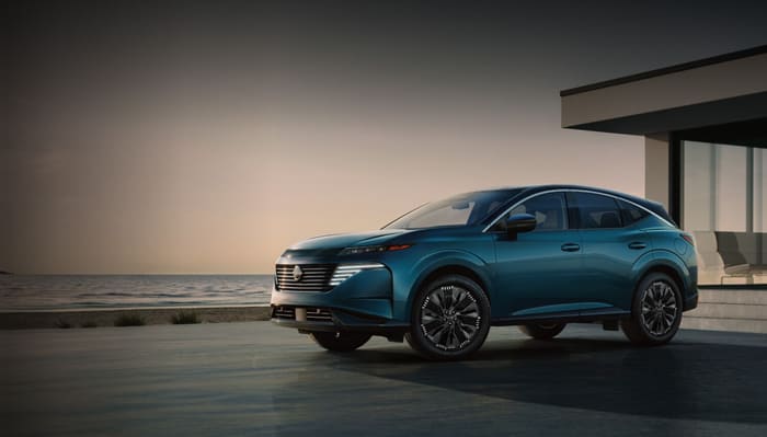 Nissan Murano 2026 en azul verdoso, vista de tres cuartos frontal, estacionada frente a una casa moderna junto al mar al atardecer